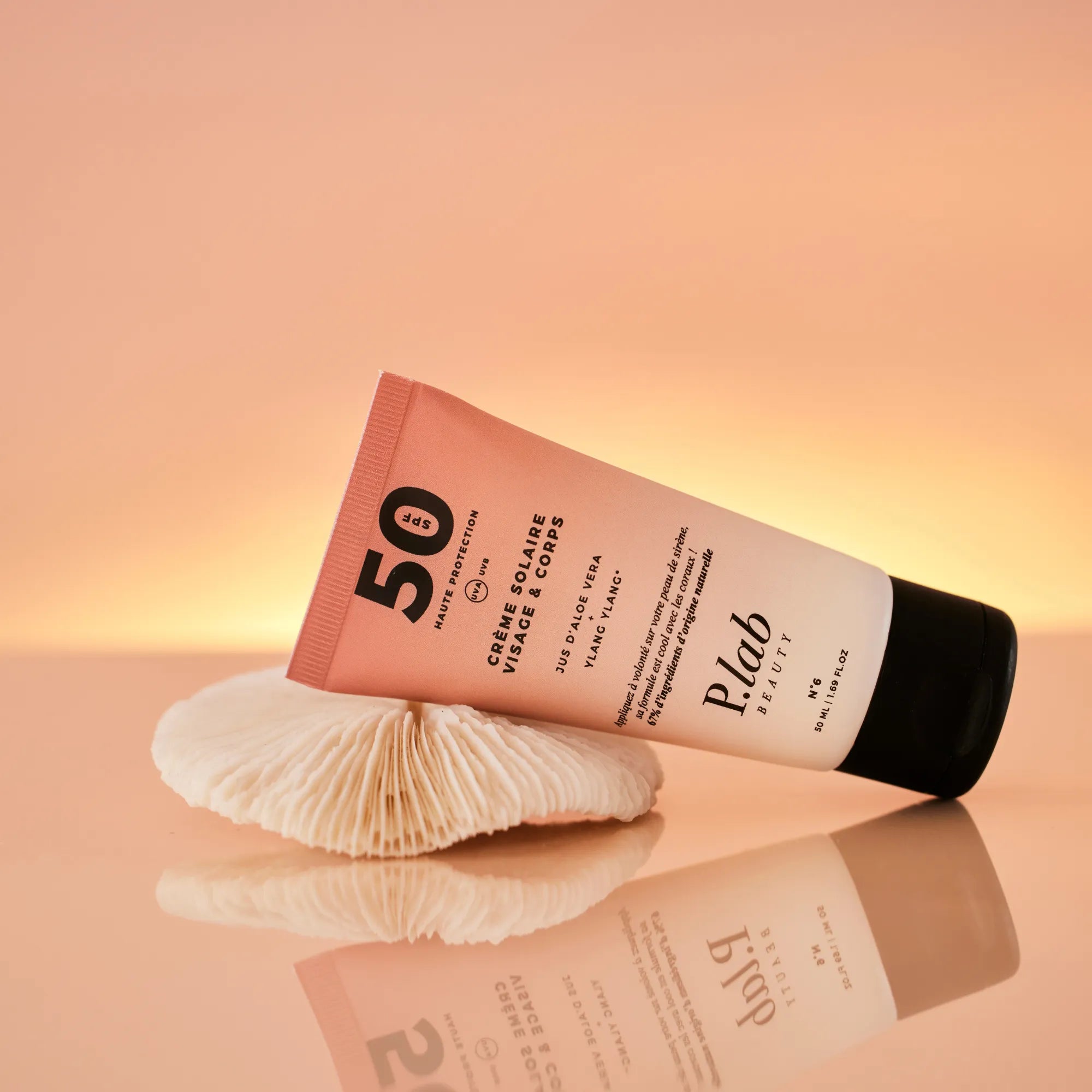 crème solaire SPF50 couchée sur coquillage fond coucher de soleil rose
