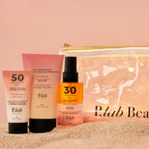 produits solaires et pochette transparente sur tas de sable fond coucher de soleil rose